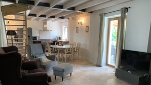 A spacious living room with a fireplace, a dining area, and a kitchen in the background. - Les Sechoirs - Gite La Riviera (Clairac)