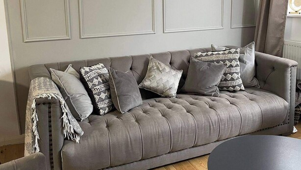 Un canapé gris recouvert de tissu, agrémenté de plusieurs coussins, est placé contre un mur orné de panneaux.