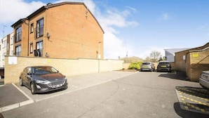 Un parking avec un bâtiment en briques, une voiture et un petit panneau.