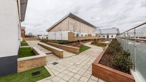 Un bâtiment moderne doté d’un toit plat, de grandes fenêtres et d’une cour intérieure agrémentée de jardinières et d’un chemin bordé de carreaux.
