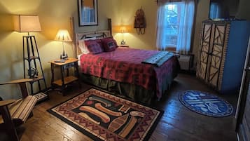 Un dormitorio acogedor con cama, dos lámparas de noche, una ventana con cortinas, suelo de madera y alfombra estampada.