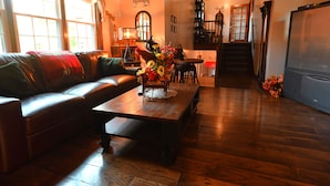 A cozy living room with a leather sofa, a wooden coffee table with a vase of flowers, and a staircase leading to an upper level.