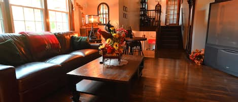 Una sala de estar acogedora con un sofá de cuero, una mesa de centro de madera con un jarrón de flores y una escalera que conduce a un nivel superior.