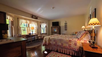 A cozy bedroom with a bed, a desk, and a chair. There is a window with curtains and a lamp on the bedside table.
