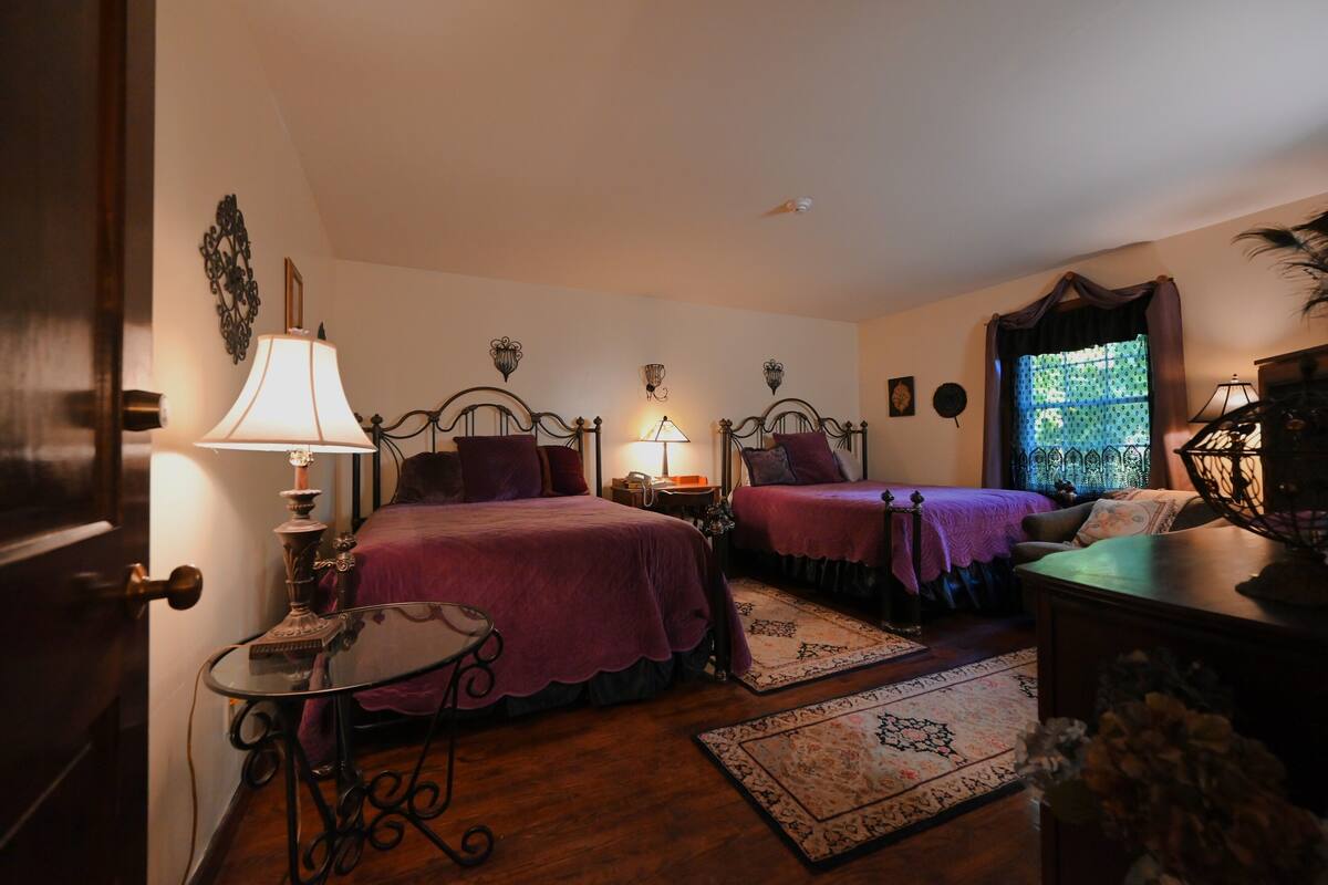 A bedroom with two beds, a small table, a lamp, and a window with curtains.