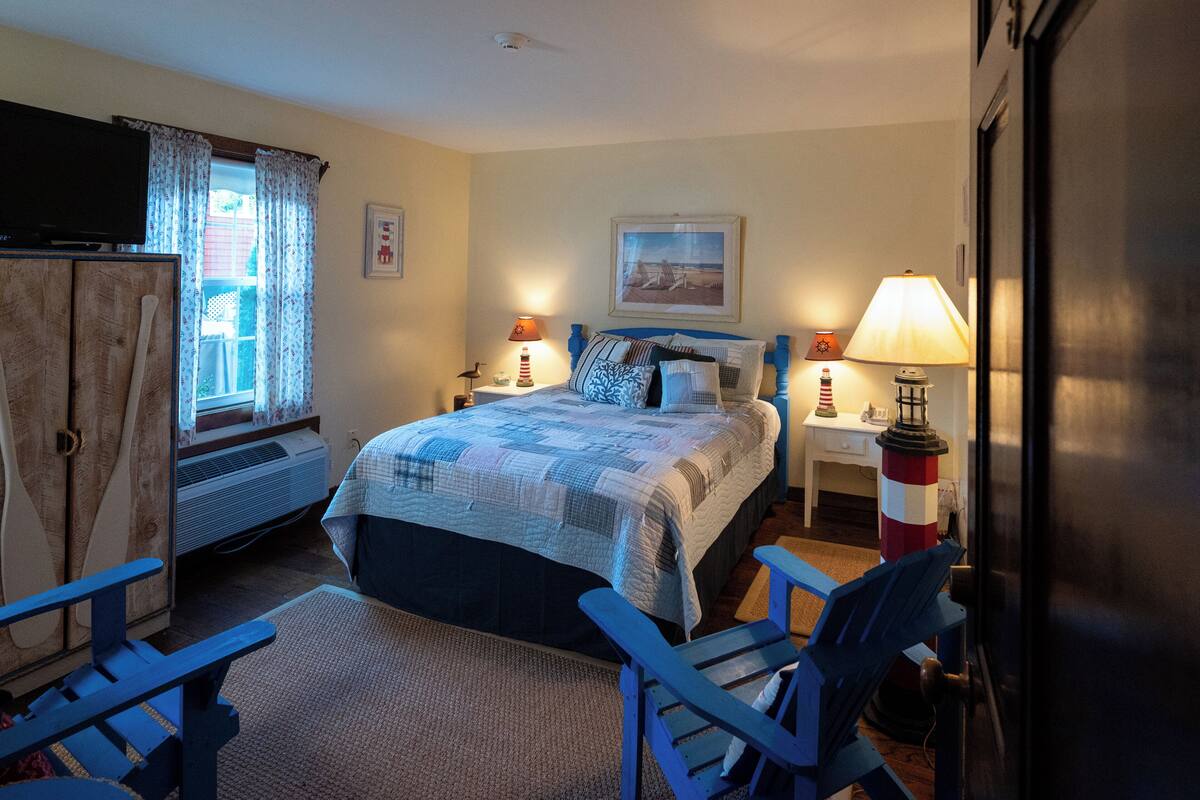 A bedroom with a bed, two bedside tables with lamps, a television, a window with curtains, and a small chair.
