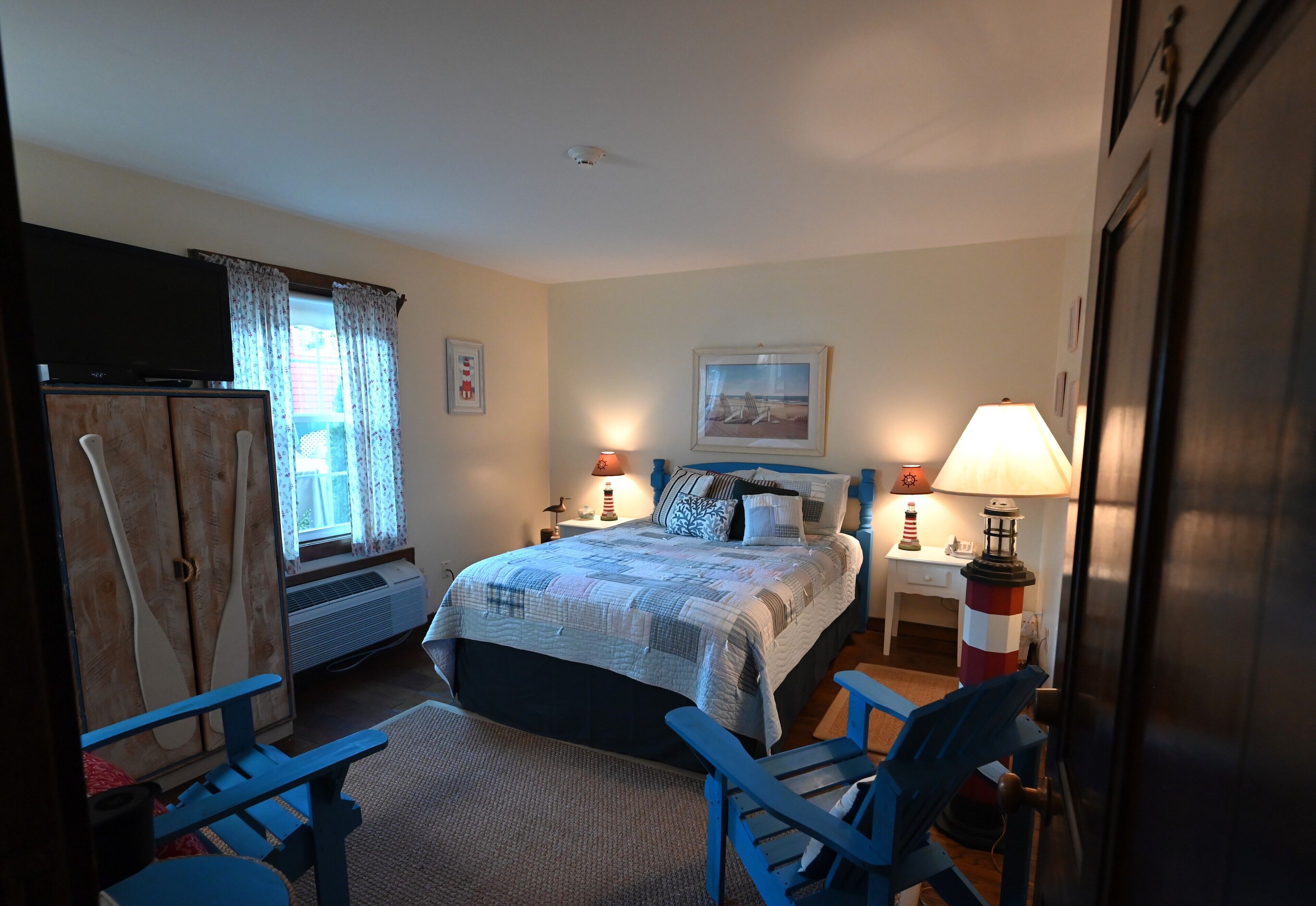 A bedroom with a bed, two bedside lamps, a desk, a chair, a wardrobe, and a television.