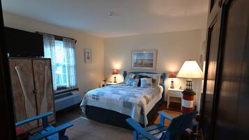 A bedroom with a bed, two bedside lamps, a desk, a chair, a wardrobe, and a television.