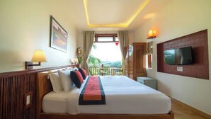 A hotel room with a large bed, a TV mounted on the wall, a balcony with a view, and a wooden headboard. - Deluxe Double Room with Balcony, Lake, River View (Hoi An)