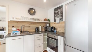 A modern kitchen with white cabinets, a built-in oven, a microwave, and a refrigerator. There is a clock on the wall and a coffee machine on the counter.