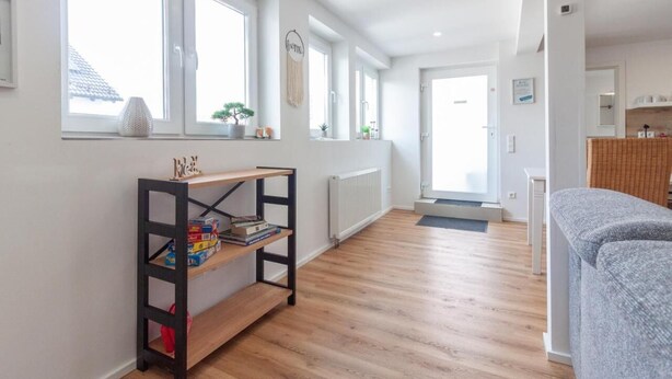 A bright, open-plan living space with a wooden floor, a bookshelf, and a grey sofa.