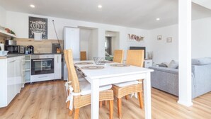 A modern kitchen with white cabinets, a built-in oven, and a dining area with a white table and wicker chairs.