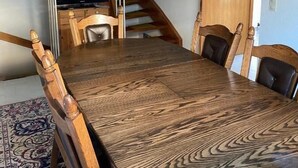 Een eetkamer met een grote houten tafel, stoelen, een televisie en een trap.