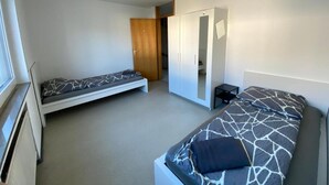Een kleine kamer met twee eenpersoonsbedden, een kledingkast en een klein nachtkastje.