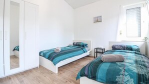 A bedroom with two beds, a wardrobe, a small table, and a window. - nJoy! Sunny Apartment Göppingen | Balcony & Parking (Göppingen)