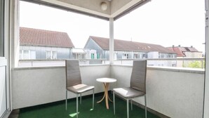 A balcony with two chairs and a small table, a green artificial turf floor, and a view of neighboring houses. - nJoy! Sunny Apartment Göppingen | Balcony & Parking (Göppingen)