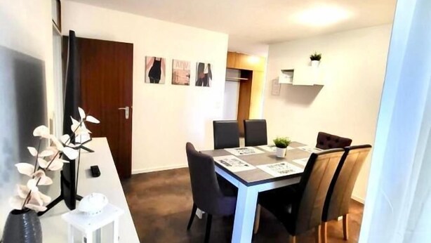 Ein Essbereich mit Tisch und Stühlen, einer kleinen Pflanze an der Wand und einer Tür im Hintergrund.