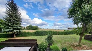 Ein Garten mit einer Holzterrasse, einer großen Nadelbaum und einer Hecke.