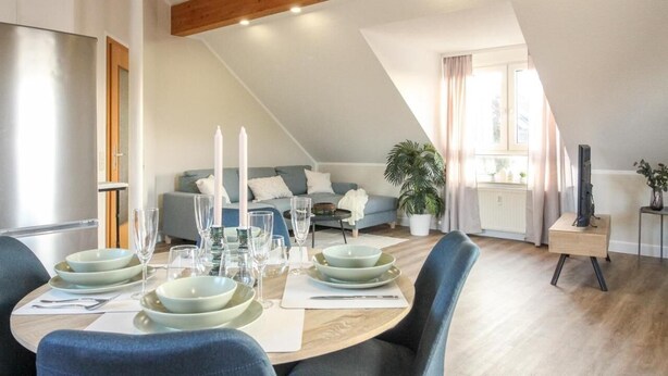 Un comedor con una mesa redonda para cuatro personas, un sofá al fondo y un televisor sobre un mueble.