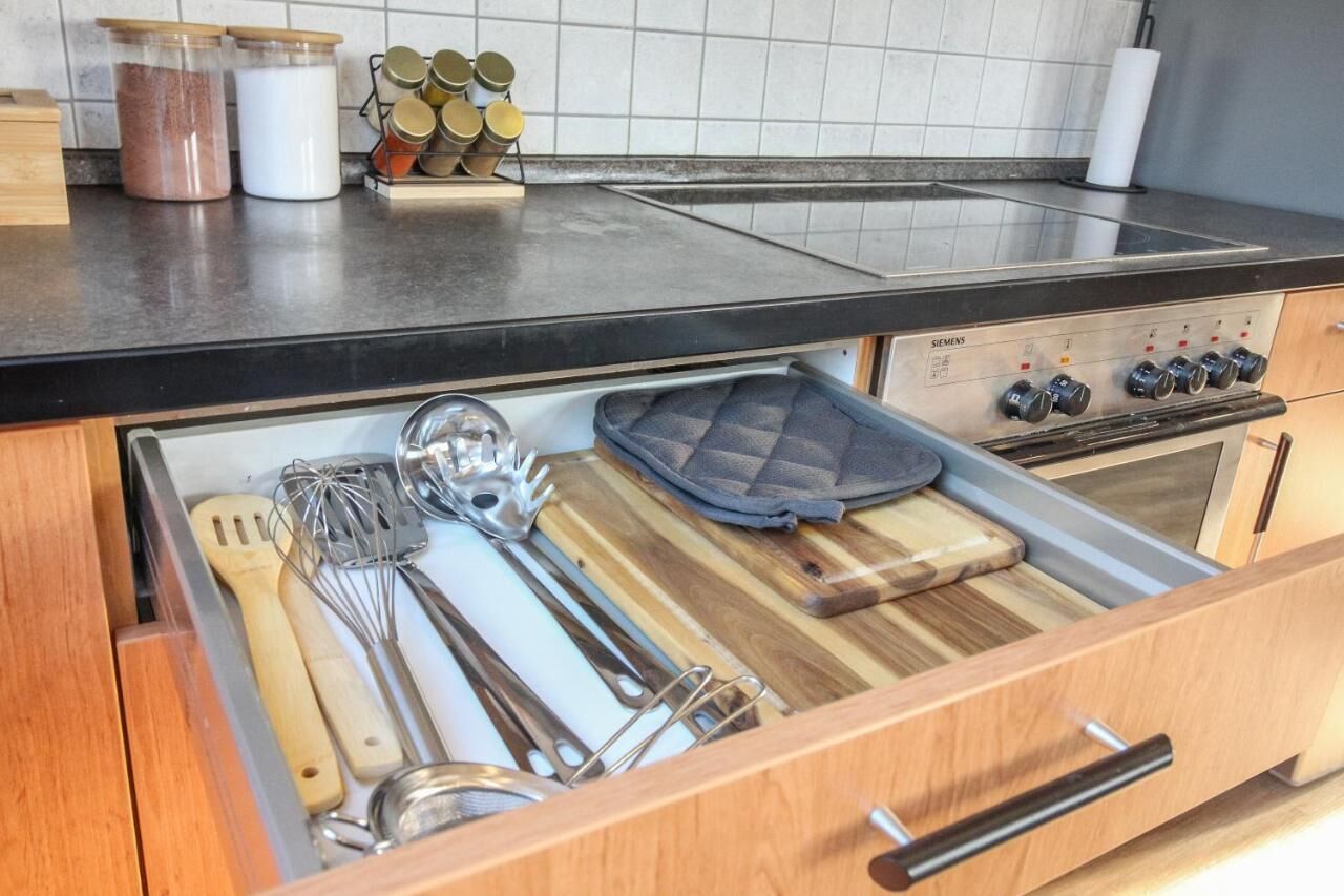 Una cocina con un cajón de madera que contiene utensilios de cocina, una tabla de cortar y una bandeja para hornear.