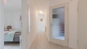 Un corridoio stretto con un letto a sinistra e una porta con vetro smerigliato a destra.