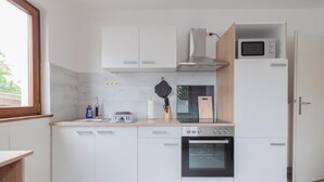 Una cucina compatta con mobili bianchi, un forno a microonde, un fornello e un forno integrato.