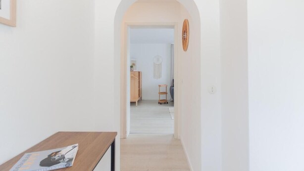 Un corridoio con un tavolo di legno e un quadro incorniciato, che conduce a una stanza con un armadio e un tavolino.