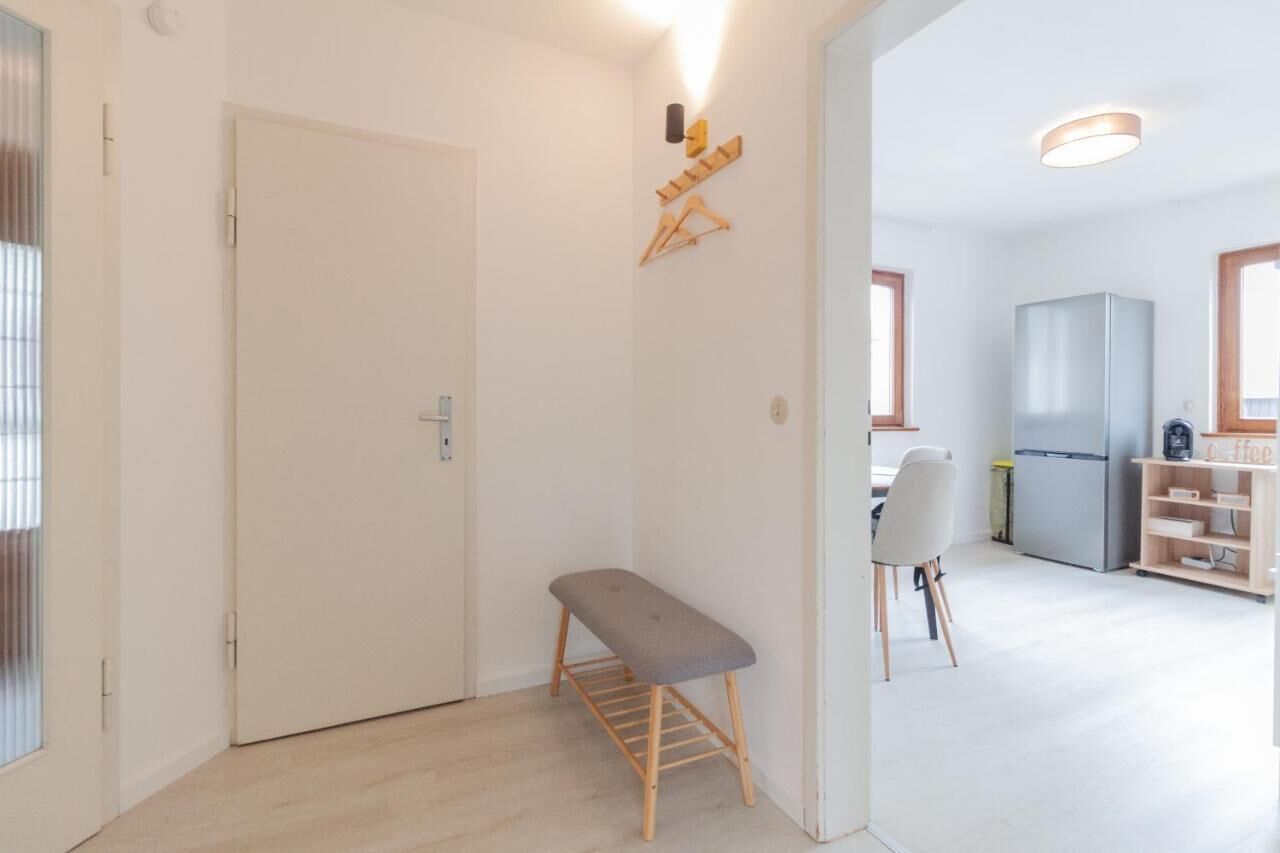 A modern apartment with a minimalist design, featuring a bench, a kitchen area with a refrigerator, and a dining table.