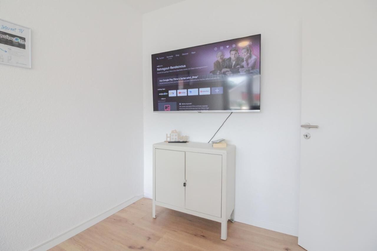 Un téléviseur à écran plat fixé au mur, au-dessus d’un meuble blanc sur lequel est posée une petite table.