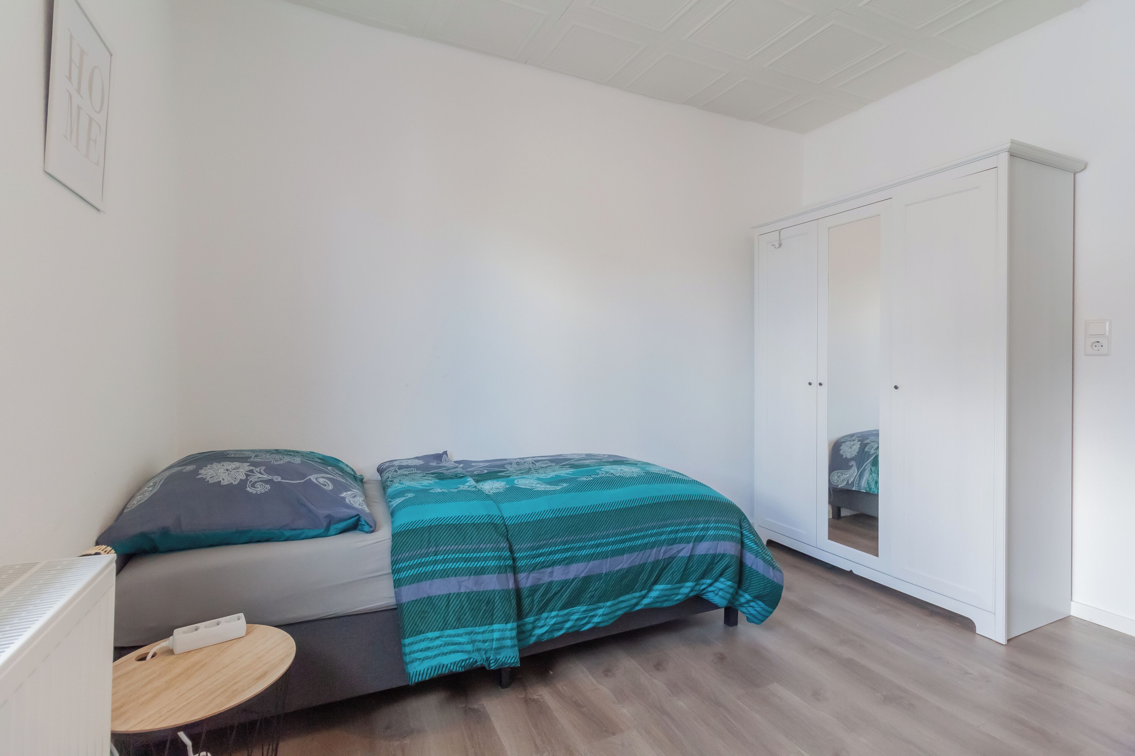 A bedroom with a bed, a bedside table, a wardrobe, and a mirror.