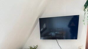 Een keuken met houten kastjes, een magnetron, een waterkoker en een flatscreen televisie aan de muur.