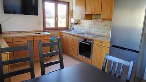 Een keuken met houten kastjes, een zwart aanrecht, een roestvrijstalen koelkast, en een flatscreen televisie aan de muur.