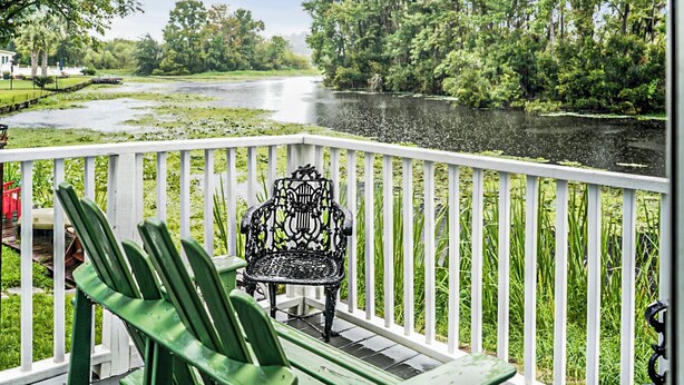 A balcony with a chair, overlooking a river with trees and a building in the background.