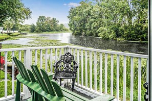 A balcony with a chair, overlooking a river with trees and a building in the background.