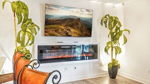 A modern living room with a fireplace, a mounted TV, and two potted plants.