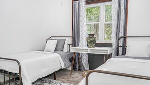 A bedroom with two single beds, a small table with a vase, and a window with curtains.