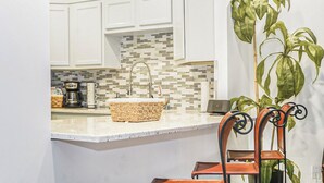 A kitchen with white cabinets, a tiled backsplash, a sink, and a coffee maker.