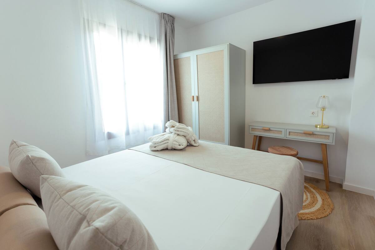 Una habitación de hotel con cama, escritorio, televisor y ventana con cortinas.