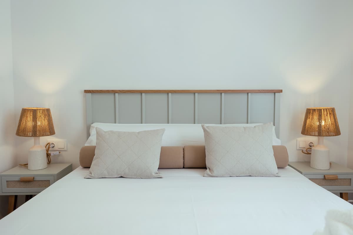 Una cama bien tendida con dos almohadas, un cabecero de madera y dos lámparas de noche a cada lado.