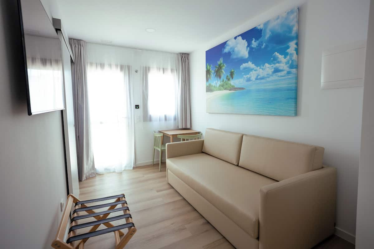 Una sala de estar moderna con un sofá color beige, un tendedero de madera, una mesita pequeña y un cuadro con una escena de playa.