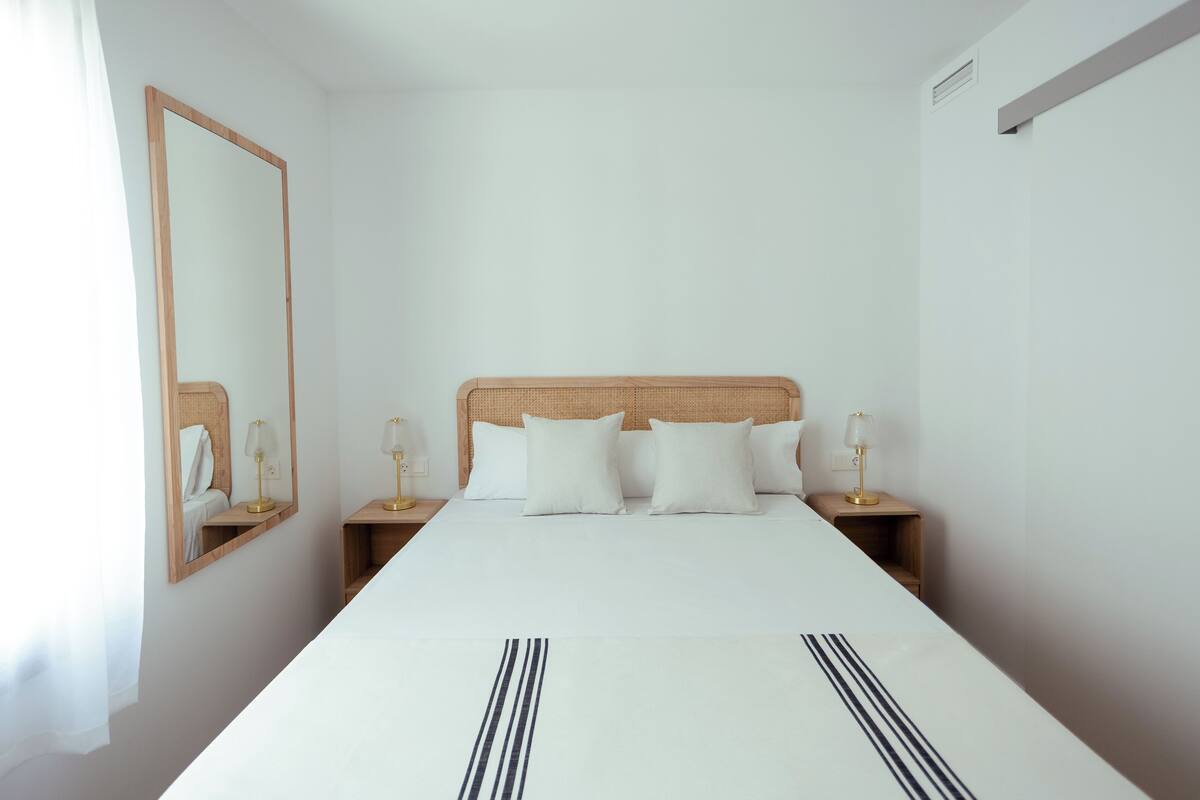 Una habitación de hotel con una cama grande, dos mesitas de noche, un espejo y una mesita con lámpara.
