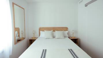 A hotel room with a large bed, two bedside tables, a mirror, and a nightstand with a lamp.