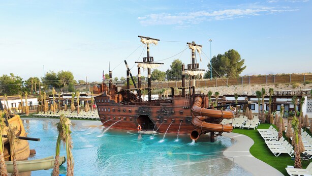 A large pool with a pirate ship structure, surrounded by lounge chairs and palm trees. - Magic Pirates Island Resort (Benidorm)