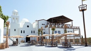 A white building with a bell tower, outdoor seating with umbrellas, and a wooden deck. - Magic Pirates Island Resort (Benidorm)