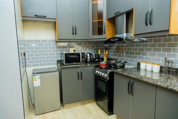 Cocina compacta con gabinetes grises, microondas integrado, estufa y refrigerador pequeño.