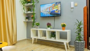 Un salon moderne avec un téléviseur fixé au mur, une console blanche agrémentée de plantes en pot et un plancher en bois.