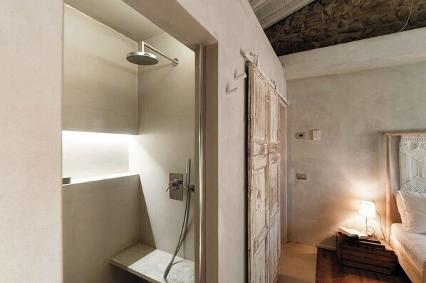 A modern bathroom with a shower, a bedside table with a lamp, and a rustic door.