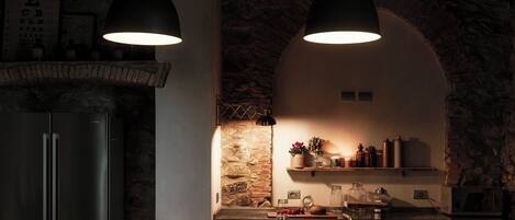 A modern kitchen with a stone wall, two pendant lights, a refrigerator, a sink, and a wine glass on the counter.