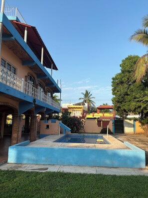 A courtyard with a swimming pool, a multi-story building with balconies, and a clear blue sky. - Amplia casa de 6 cuartos, alberca, aire acondicionado, y WiFi. (La Peñita de Jaltemba)