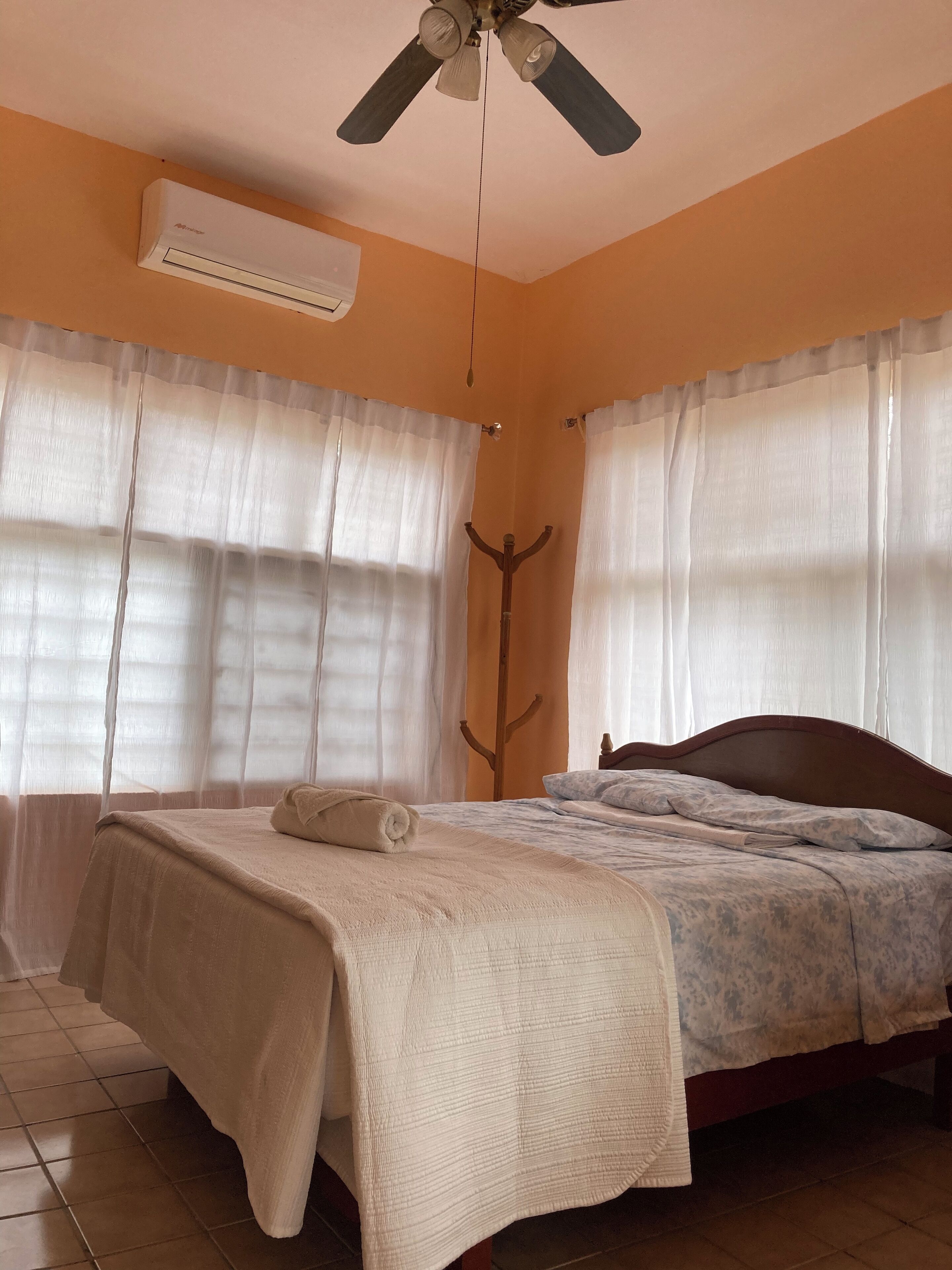 Una camera da letto con un letto, una ventola a soffitto, un condizionatore d'aria e tende leggere.